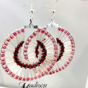 May include: A pair of silver hoop earrings with a beaded design. The beads are clear, pink, and black. The earrings are handmade and have a unique, modern design.