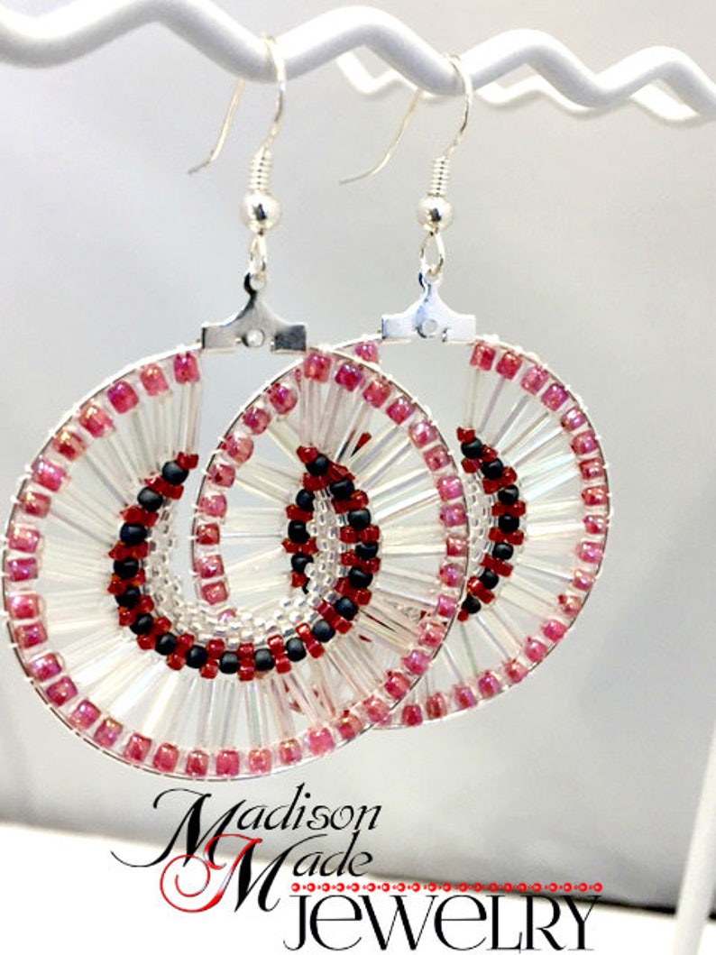 May include: A pair of silver hoop earrings with a beaded design. The beads are clear, pink, and black. The earrings are handmade and have a unique, modern design.
