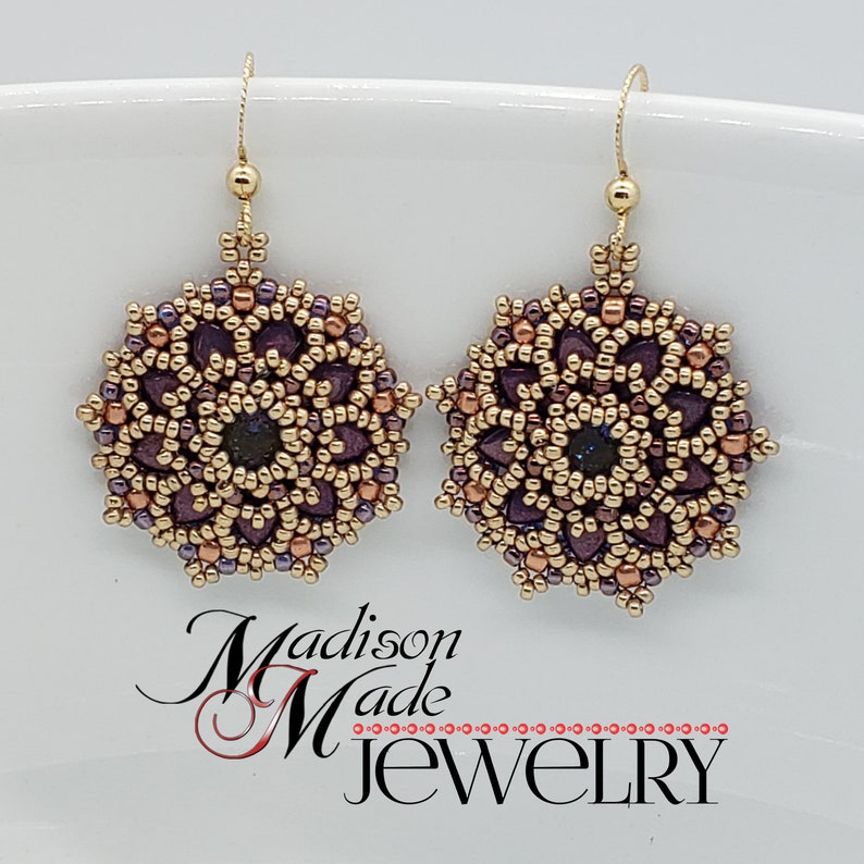 May include: A pair of beaded earrings with a floral design. The earrings feature a gold-colored metal with purple and bronze beads. The center of each earring has a dark blue bead. The earrings are labeled "Madison Made Jewelry".