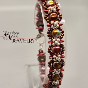 May include: A beaded bracelet with brown, red, and silver beads. The bracelet is on a clear display stand.