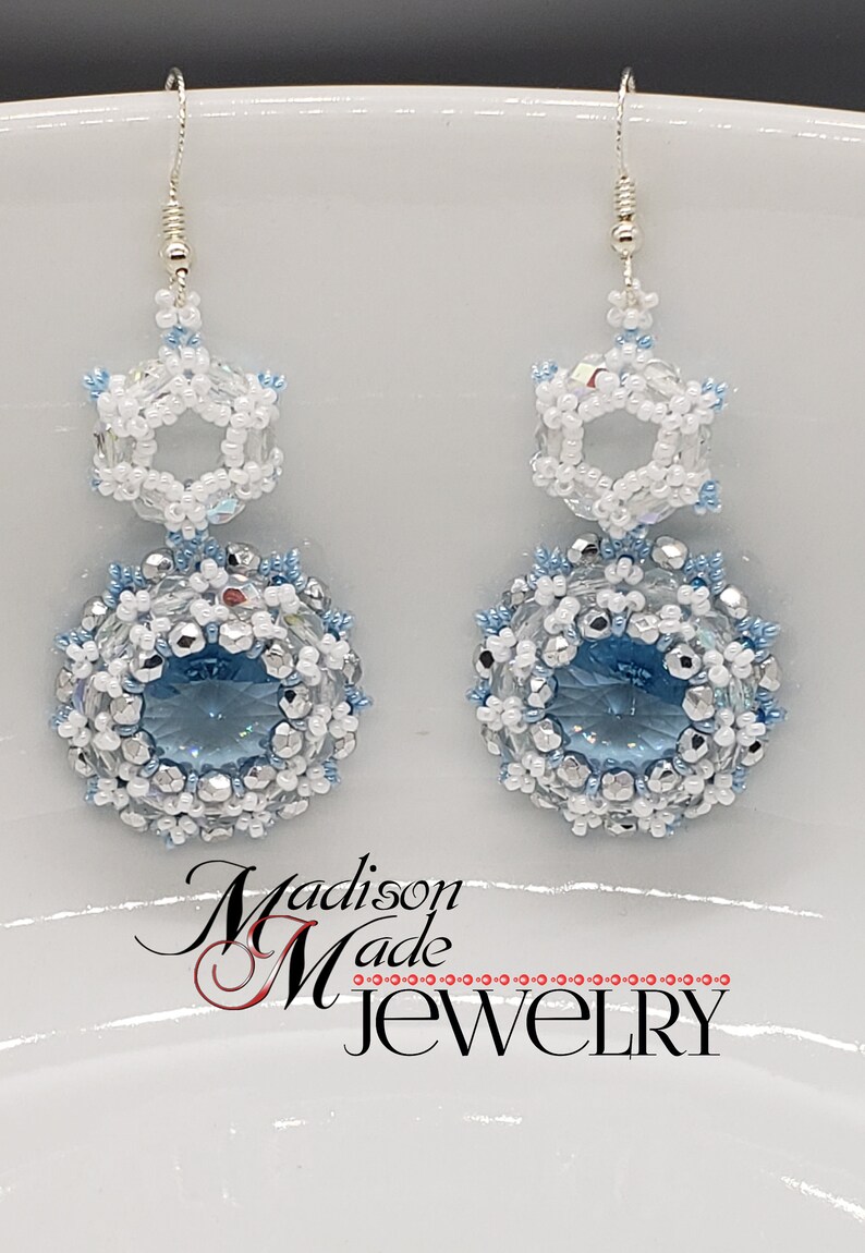 May include: A pair of silver snowflake earrings with blue and white crystal beads. The earrings are made by Madison Made Jewelry.