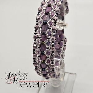 May include: A purple and silver beaded bracelet with a clasp closure. The bracelet is made with a variety of beads, including square, round, and faceted beads.