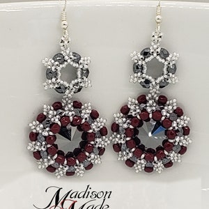 May include: A pair of silver earrings with a burgundy and silver bead design. The earrings feature a hexagonal bead surrounded by smaller beads in a snowflake pattern.