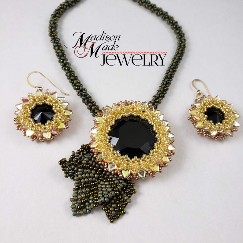 May include: A black and gold beaded necklace with a large black gemstone pendant and matching earrings. The necklace features a green beaded chain and a bow-shaped pendant. The earrings are small and round with a black gemstone center.
