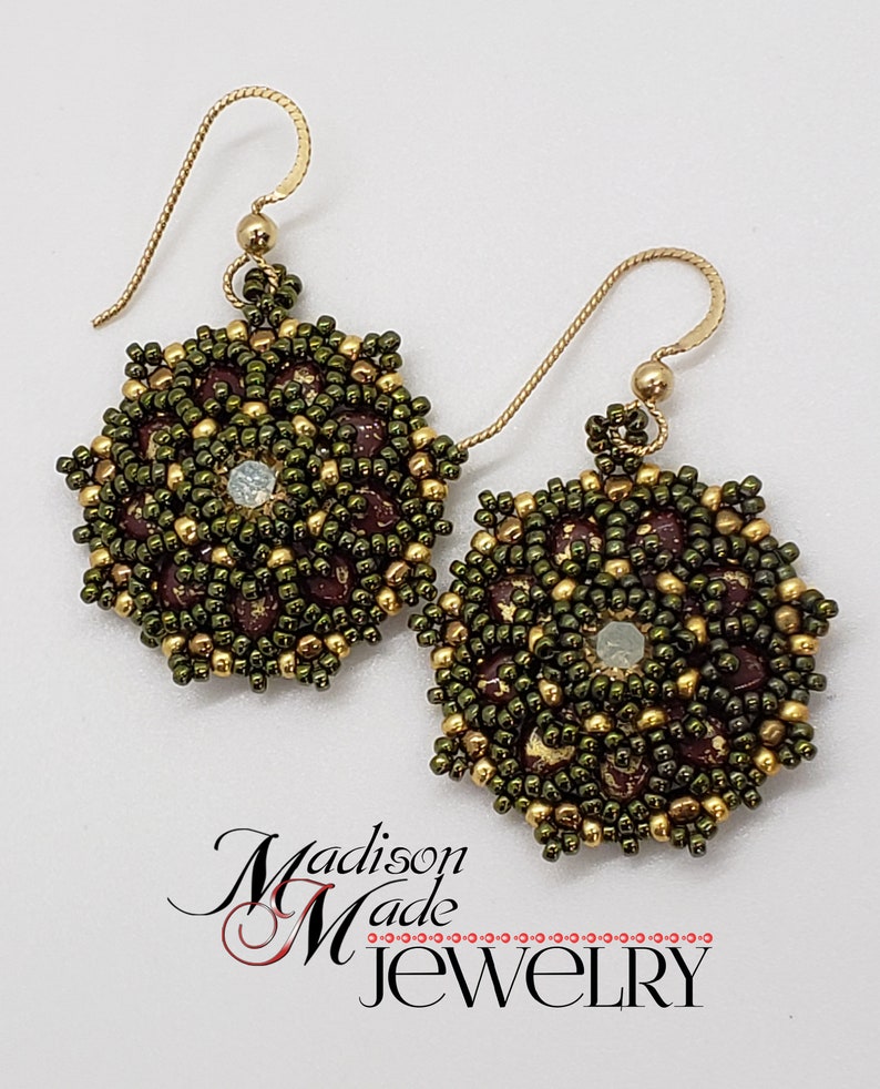 May include: A pair of handmade beaded earrings. The earrings feature a circular design with olive green, gold, and burgundy beads. Each earring has a gold-colored hook and a small, iridescent bead in the center. The earrings are displayed on a white background.
