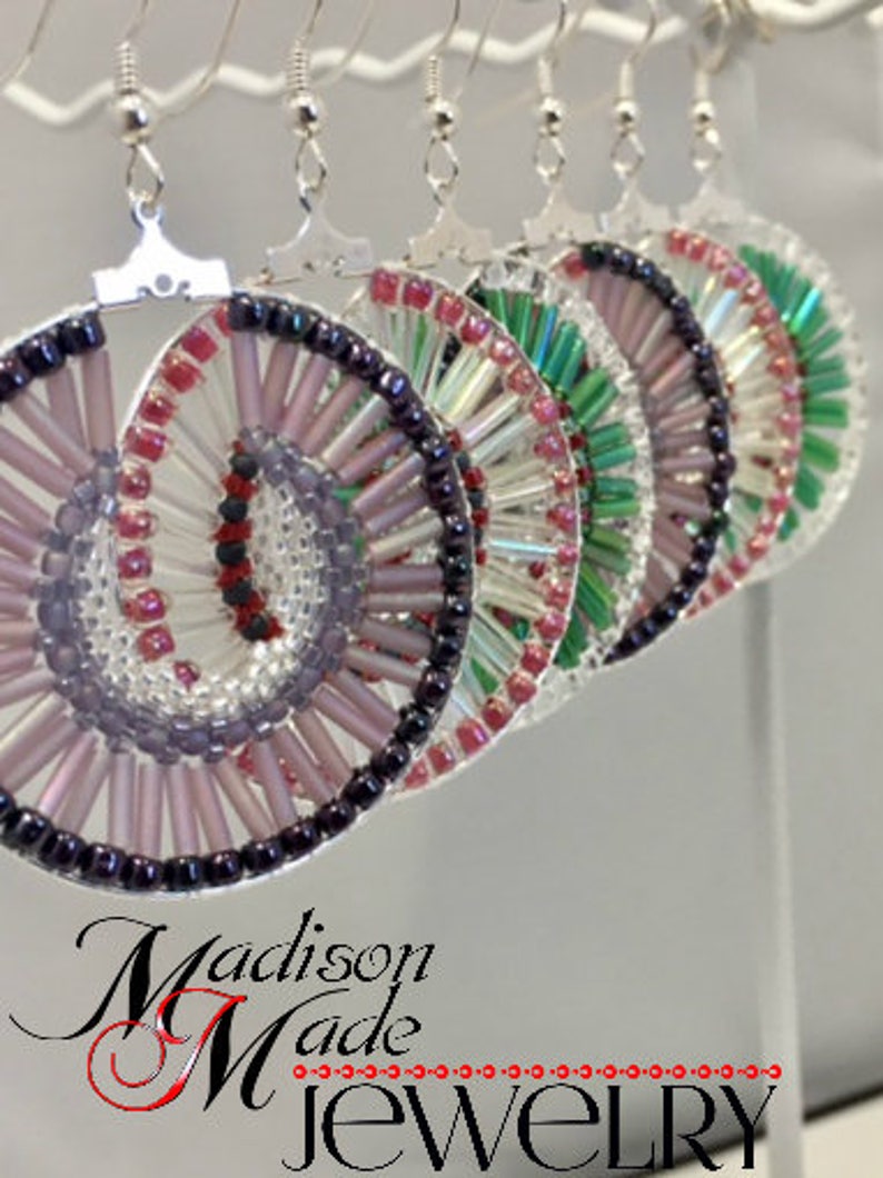 May include: A set of four pairs of earrings with a spiral design. The earrings are made of silver and glass beads in shades of pink, purple, green, and white. The earrings are hanging from a white background.