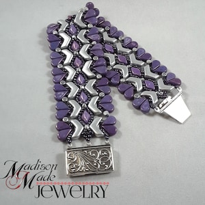 May include: A purple and silver beaded bracelet with a silver clasp and a decorative silver charm. The bracelet is made with a chevron pattern and has a heart-shaped bead design.