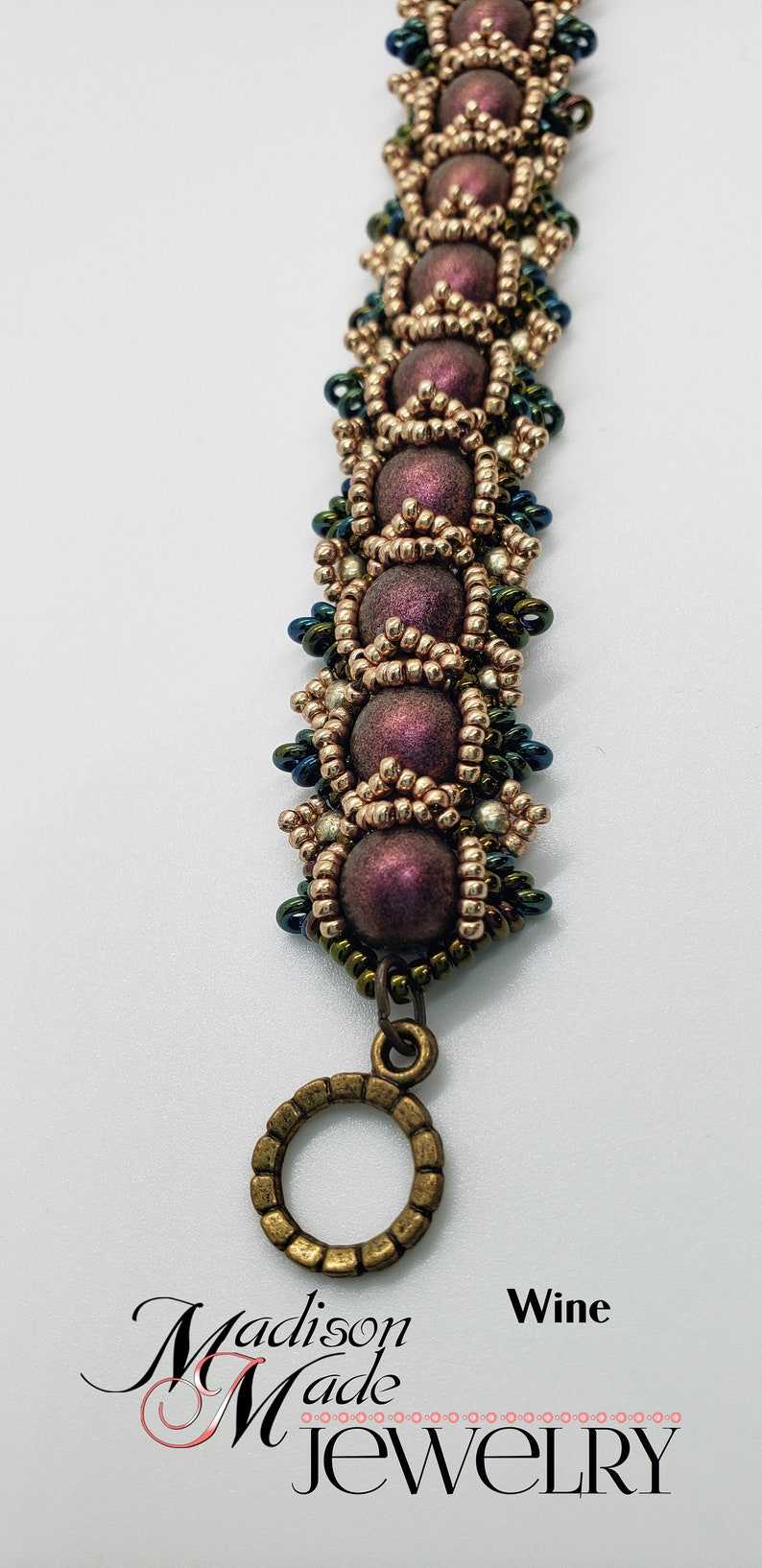 May include: A beaded bracelet with a bronze clasp. The beads are a mix of gold, silver, and dark purple. The bracelet is labeled "Wine".
