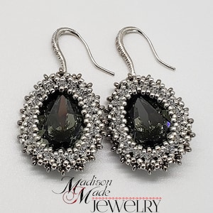 May include: A pair of silver dangle earrings with a teardrop-shaped dark gray crystal surrounded by silver and clear beads.