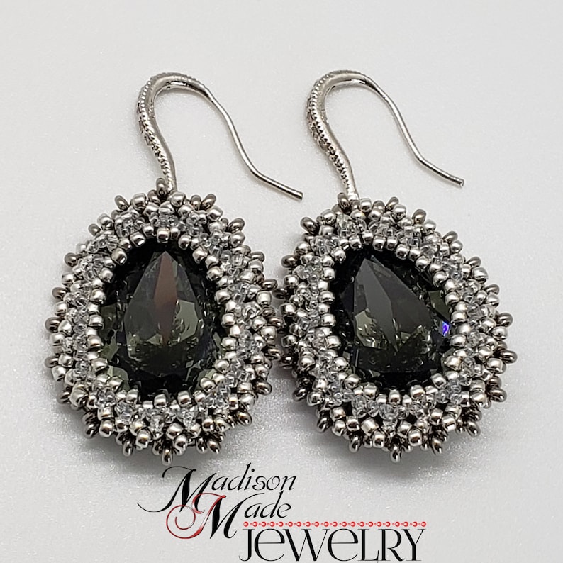 May include: A pair of silver dangle earrings with a teardrop-shaped dark gray crystal surrounded by silver and clear beads.