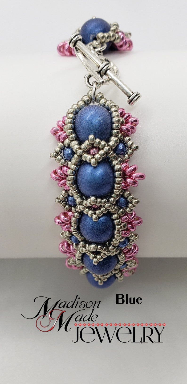 May include: A blue beaded bracelet with silver and pink beads. The bracelet has a toggle clasp. The bracelet is made by Madison Made Jewelry.