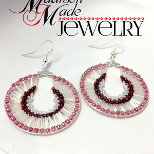 May include: A pair of hoop earrings with a beaded design. The earrings are made with white, pink, and black beads. The earrings are hanging from silver hooks.