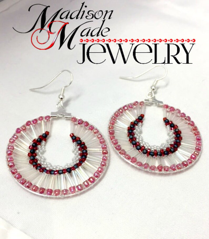 May include: A pair of hoop earrings with a beaded design. The earrings are made with white, pink, and black beads. The earrings are hanging from silver hooks.