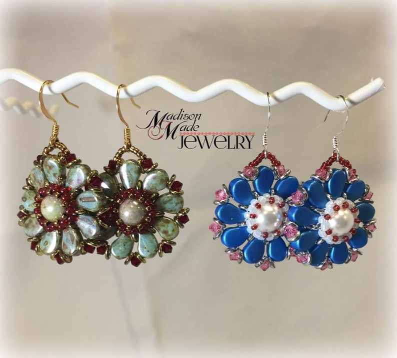 May include: Two pairs of beaded earrings, one pair is blue and white with a pearl center, the other pair is green and red with a pearl center. The earrings are hanging from a white display stand. The text "Madison Made Jewelry" is visible in the background.