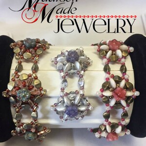 May include: Three beaded bracelets with floral designs. The bracelets are made with white, pink, and purple beads. The bracelets are displayed on a white surface with the text "Madison Made Jewelry" above them.