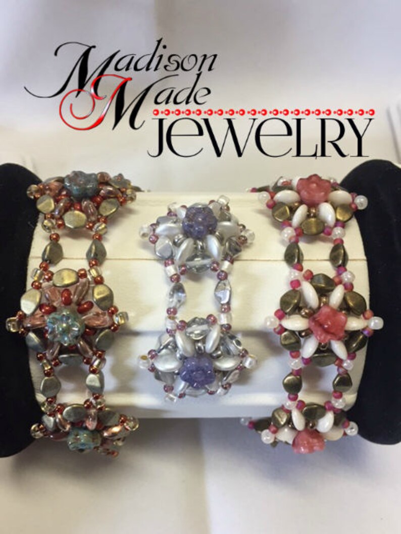 May include: Three beaded bracelets with floral designs. The bracelets are made with white, pink, and purple beads. The bracelets are displayed on a white surface with the text "Madison Made Jewelry" above them.