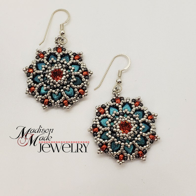 May include: A pair of handmade earrings with a floral design. The earrings feature teal, orange, and silver beads, with a red center stone. The earrings are suspended from silver hooks. The text "Madison Made Jewelry" is in the lower left corner.