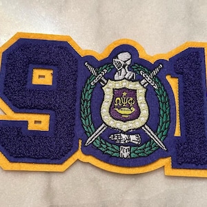 May include: A purple and gold felt patch with the year 1911 and a crest with a knight and swords.