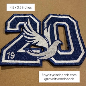 May include: A navy blue and white embroidered patch, measuring 4.5 x 3.5 inches. The patch features the number "20" with a dove in the center and the number "19" at the bottom. The text "Royaltyandbeads.com @royaltyandbeads" is at the bottom.