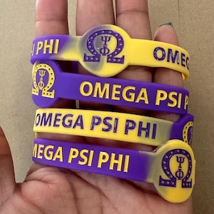 May include: Four purple and yellow silicone bracelets with the text "OMEGA PSI PHI" and a Greek letter symbol.