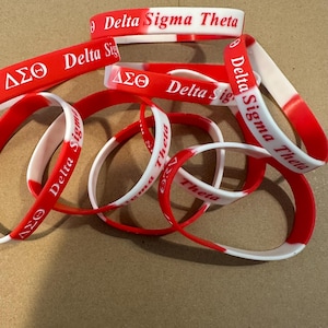 May include: A group of red and white silicone bracelets with the text "Delta Sigma Theta" printed on them.