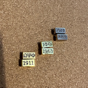 May include: Four gold-colored metal blocks with engraved text. The blocks read "1911", "ΩΨΦ", "1911", and "1963". Two silver-colored metal blocks read "1911" and "ΚΔΨ".