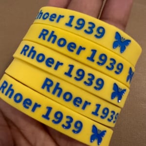 May include: Five yellow silicone wristbands with blue text and a blue butterfly design. Each wristband says "Rhoeer 1939".