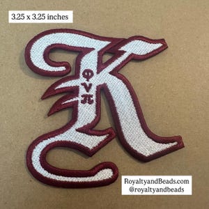 May include: Embroidered patch in the shape of a stylized letter "K", measuring 3.25 x 3.25 inches. The patch features a white embroidered design with a maroon border and accents. The Greek letters Φ, ∇, and π are embroidered in the center.