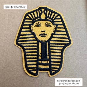 May include: Embroidered patch featuring the stylized face of an Egyptian pharaoh, with a yellow background and black details. The patch measures 4 x 3.25 inches. The patch has the text "Royaltyandbeads.com @royaltyandbeads".