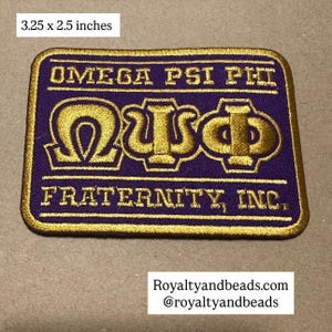 May include: A rectangular patch, 3.25 x 2.5 inches, with the words "OMEGA PSI PHI FRATERNITY, INC." in gold lettering on a purple background. The patch features the Greek letters Omega, Psi, and Phi in gold.