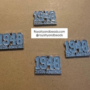 May include: Four light blue and silver metal pins. Each pin has the number "1948" in a bold font, with the words "ZETA AMICAE" below. The website "Royaltyandbeads.com" and Instagram handle "@royaltyandbeads" are also visible.