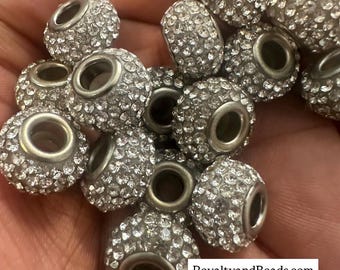 May include: A collection of silver-toned beads encrusted with sparkling rhinestones. Each bead has a large central hole and is spherical or cylindrical in shape. The beads are clustered together, showcasing their reflective surfaces. Text on the image reads: RoyaltyandBeads.com @royaltyandbeads.