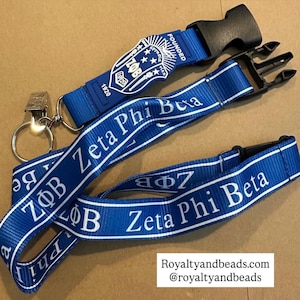 May include: Blue lanyards with white text that reads "Zeta Phi Beta". One lanyard has a black plastic clasp and a metal clip with a key ring. The other lanyard has a shield with the text "Founded 1920".