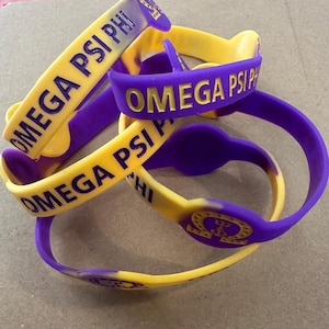 May include: Four purple and yellow silicone wristbands with the text "OMEGA PSI PHI" printed on them.