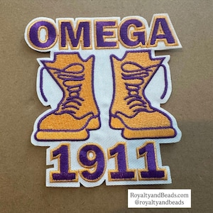 May include: Embroidered patch featuring the word "OMEGA" in purple, above a pair of orange boots with purple laces. Below the boots is the number "1911" in purple. The patch has a white background and a purple border.