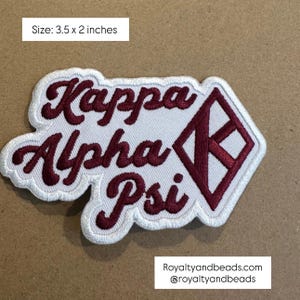 May include: Embroidered patch with the words "Kappa Alpha Psi" in burgundy script. The patch is white with a burgundy diamond-shaped design and a white border. The patch measures 3.5 x 2 inches.