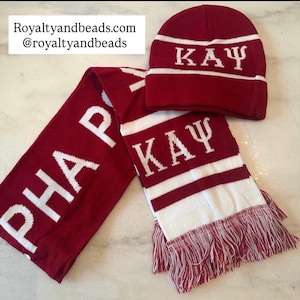 May include: A maroon knit hat and scarf set with white lettering and stripes. The hat and scarf display the Greek letters K A Y and PHA. The scarf has a fringed edge. Royaltyandbeads.com @royaltyandbeads is printed on the top left.