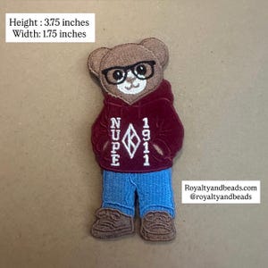 May include: An embroidered patch of a brown teddy bear wearing black glasses, a maroon hoodie with the white text NUPE 1911 and a diamond logo, blue jeans, and brown sneakers. The patch measures 3.75 inches in height and 1.75 inches in width.