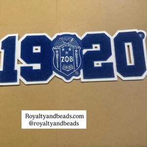 May include: A blue and white patch with the number "1920" in a bold, block letter style. The number is in blue with a white border. A crest with the letters "ZOB" and the year "1920" is in the center. The text "Royaltyandbeads.com @royaltyandbeads" is at the bottom.