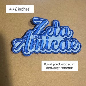 May include: A blue and light blue embroidered patch that is 4 x 2 inches. The patch features the words "Zeta Amicae" in a script font, with "1948" below the "Zeta". The website "Royaltyandbeads.com" is also visible.
