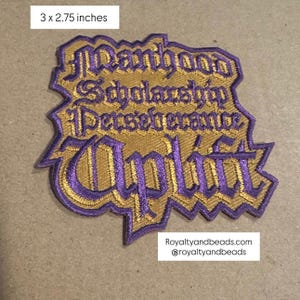 May include: Embroidered patch, 3 x 2.75 inches, with gold and purple text. The text reads "Manhood, Scholarship, Perseverance, Uplift" in a decorative font. The patch has a gold background with purple stitching.
