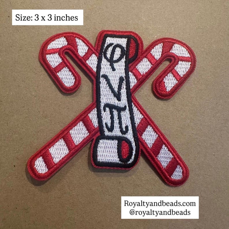 May include: A 3 x 3 inch embroidered patch featuring two red and white candy canes crossed with a vertical white banner. The banner has black Greek letters. The patch has a black border.
