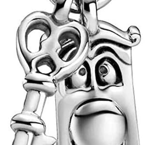 Può includere: Un ciondolo d'argento con una chiave e una porta con un viso. Il ciondolo è attaccato a un anello d'argento.