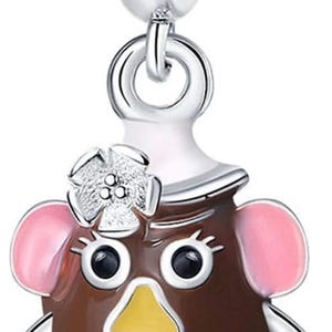 May include: A charm featuring a cartoon character with a brown body, pink ears, and red shoes. The charm has a silver bail and a flower on its head. The character has a yellow nose and a red smile.