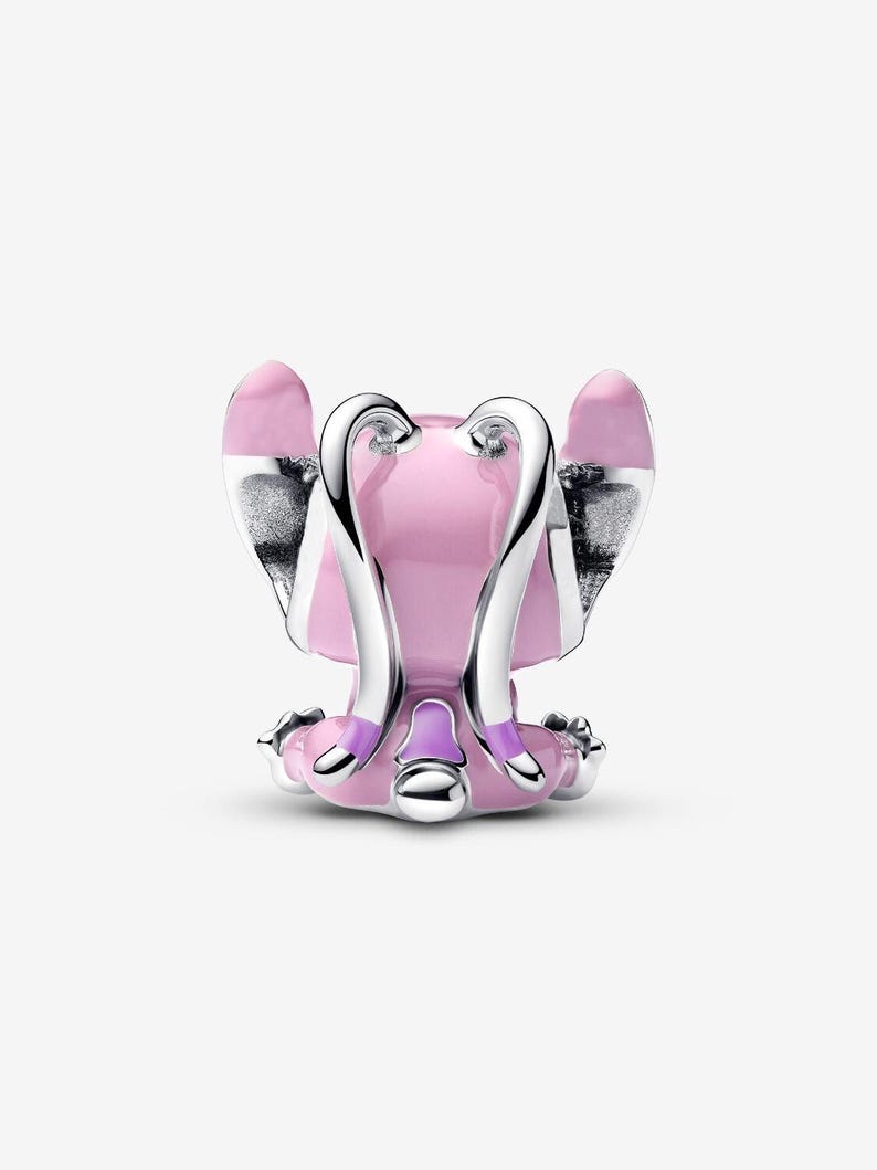 May include: A pink and silver charm featuring a stylized angel design. The charm has a pink body with silver wings and accents. The design is detailed with a smooth, polished finish, and is likely made of metal.
