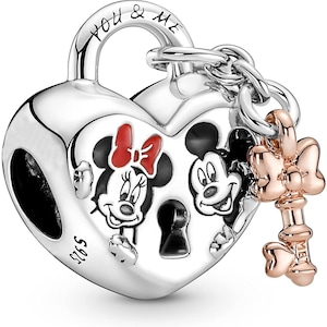 May include: Silver charm in the shape of a heart-shaped padlock with Mickey Mouse and Minnie Mouse on the front. The padlock has a keyhole and a small key charm attached to it. The key charm is rose gold and has a bow on the top. The padlock has the words "You & Me" engraved on the top.
