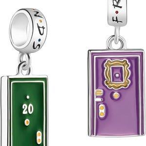 Può includere: Due braccialetti con ciondoli, uno con una porta viola con cornice dorata e l'altro con una porta verde con il numero 20. Entrambi i ciondoli sono in argento e hanno la scritta "FRIENDS" incisa su di essi.