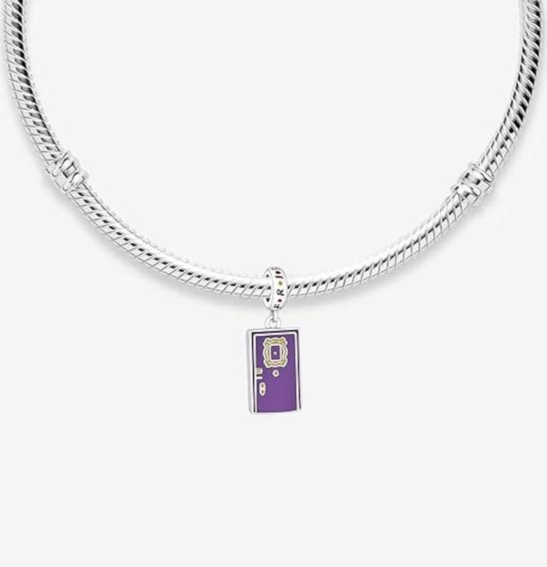 May include: A silver charm bracelet with a purple charm featuring a door with a gold frame and the words "Central Perk" in yellow letters.