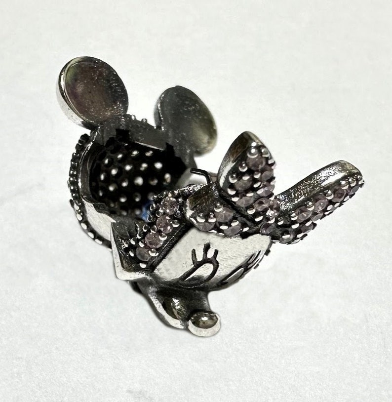 Puede incluir: Encanto de plata con un rat&oacute;n de dibujos animados con detalles de cristal rosa. El rat&oacute;n tiene orejas grandes, un lazo y una cara sonriente.