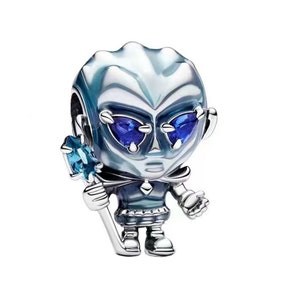 Puede incluir: Un charm plateado que representa una figura alienígena estilizada con una cabeza grande y detalles azules. La figura tiene ojos azules con forma de gema y sostiene un bastón de cristal azul. El charm es detallado y tiene una estética futurista.